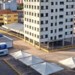 Rua em Taguatinga com hotel abandonado e barreiras para implosão, veículos de acolhimento do GDF ao fundo.