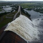 Reservatório do Descoberto transbordando no DF, expondo falhas no abastecimento hídrico com água jorrando e áreas inundadas.