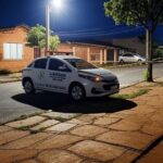 Cena de rua em Planaltina com viatura policial e fita de isolamento em frente a casa, representando investigação de crime.