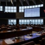 Sala de plenário vazia da CLDF com telas de transmissão ao vivo falhando, destacando ineficiências em sessão ordinária.