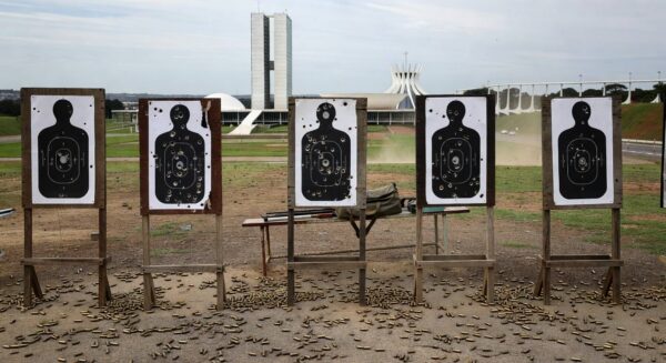 Clube de tiro vazio em Brasília com alvos perfurados e cartuchos no chão, representando temores de proliferação de armas.