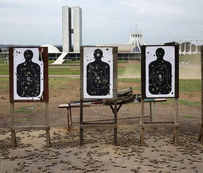 Clube de tiro vazio em Brasília com alvos perfurados e cartuchos no chão, representando temores de proliferação de armas.