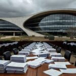 Edifício da Câmara Legislativa do DF com documentos espalhados, representando debate sobre falhas em lei contra supremacismo.