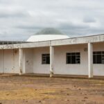 Escola pública abandonada em Brasília, com Câmara Legislativa ao fundo, destacando crises educacionais no DF.