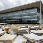 Edifício da CLDF em Brasília com documentos espalhados, representando críticas por desperdício de recursos em homenagens.