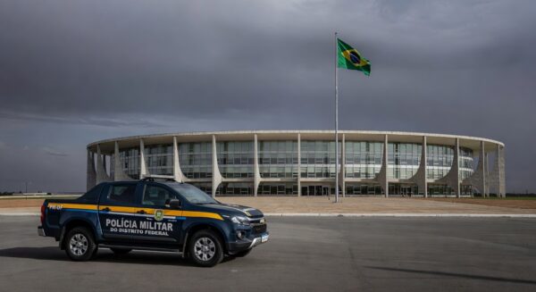 Edifício da CLDF em Brasília com viaturas da PMDF, representando discussão sobre reintegração de policiais e falhas no combate à violência contra a mulher.