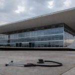 Cena de crise na saúde e segurança em Brasília, com hospital público e viaturas policiais abandonadas.