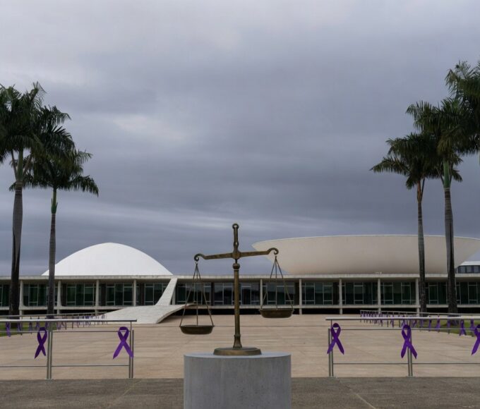 Edifício da CLDF em Brasília com símbolos de impunidade na violência de gênero, como fitas roxas e balança desequilibrada.
