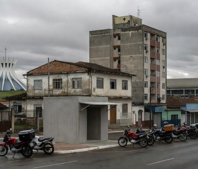 Rua em Brasília com motos de motofretistas perto de ponto de apoio, expondo negligência após demora de oito anos.